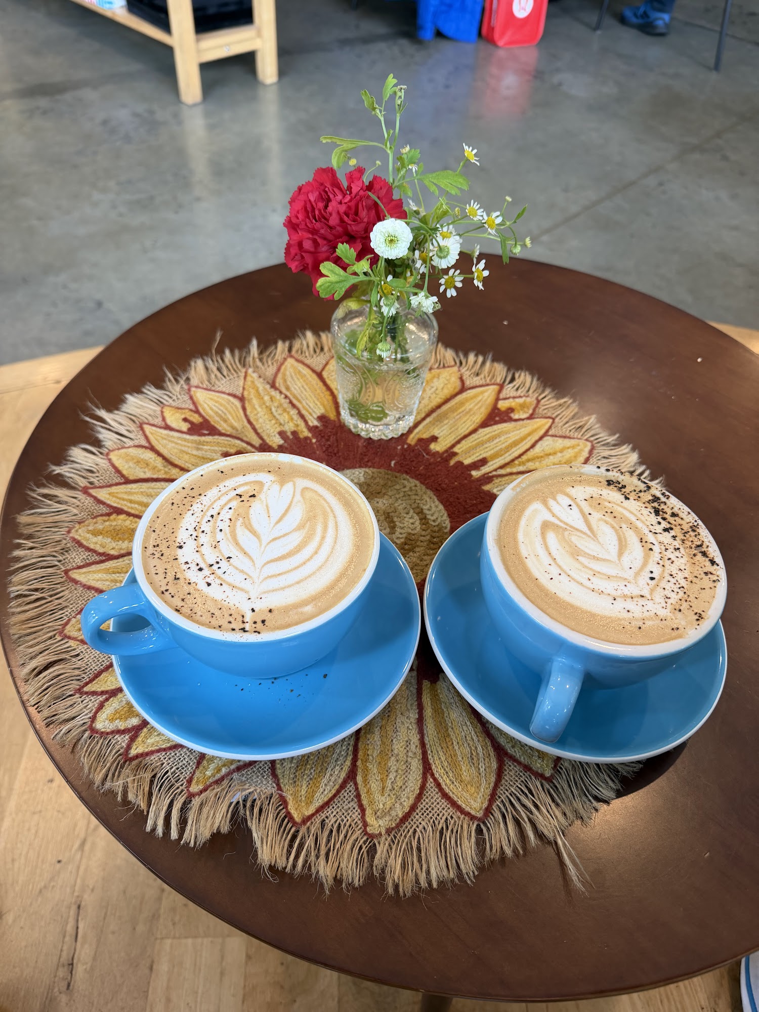 Two blue coffee cups, flowers, and a patterned textile on a cafe table